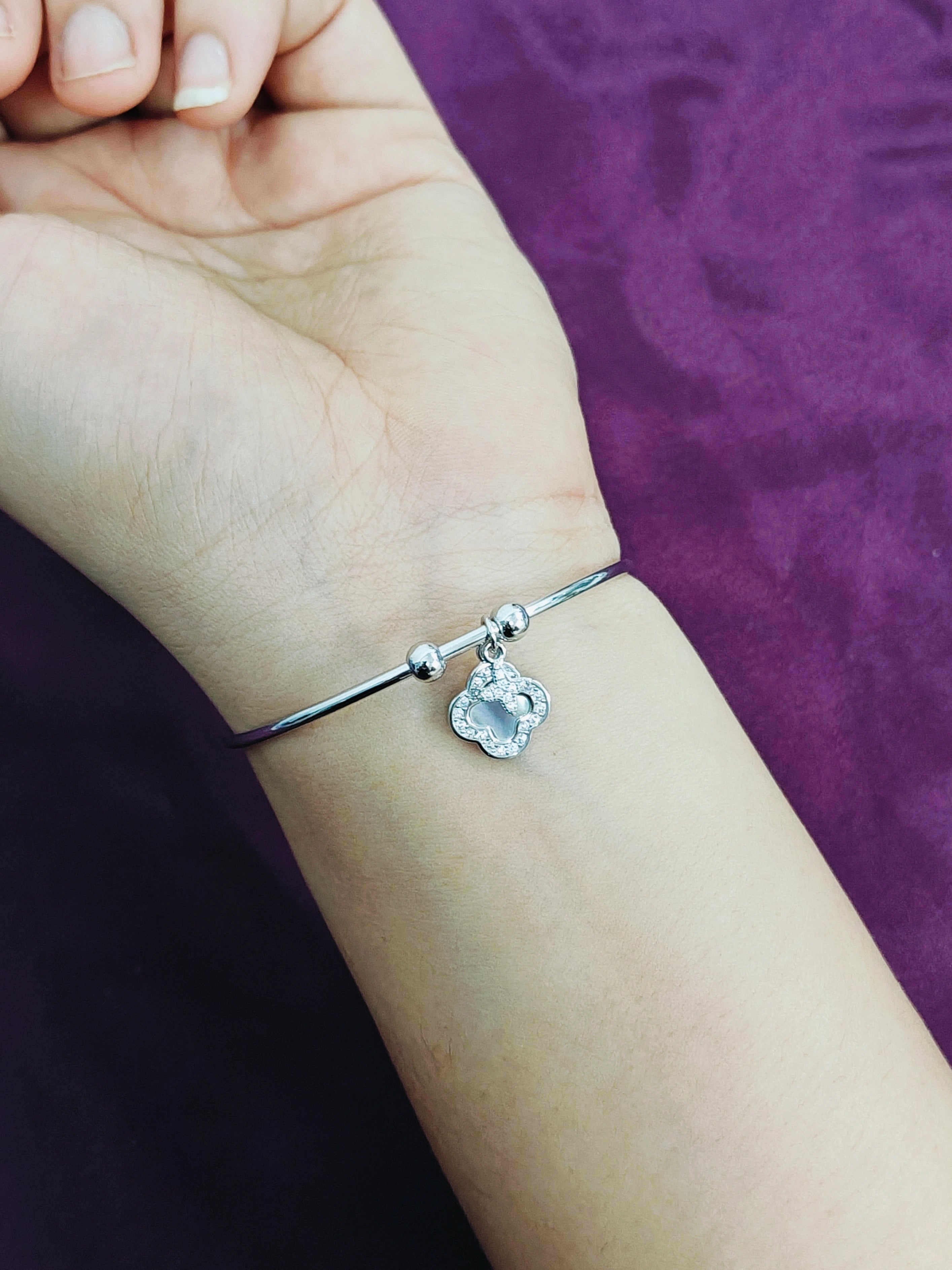 Silver bracelet with a heart-shaped charm on a wrist against a purple background